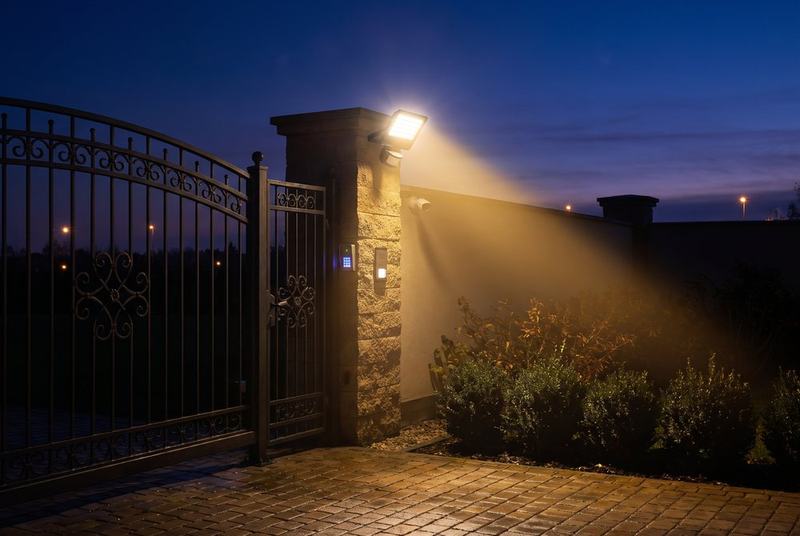 Secure home gate with motion-sensor floodlight at dusk